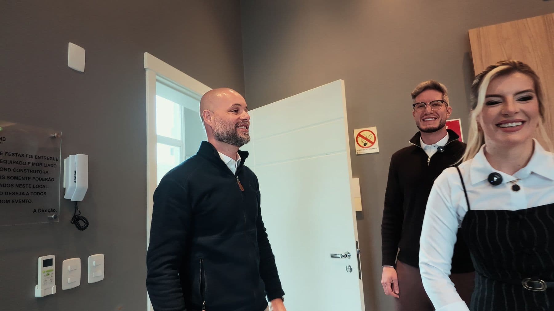 Paulo Tasca Bortolini chega ao estúdio recebido por Joceane Lenhart e Ícaro Piacini, todos sorrindo