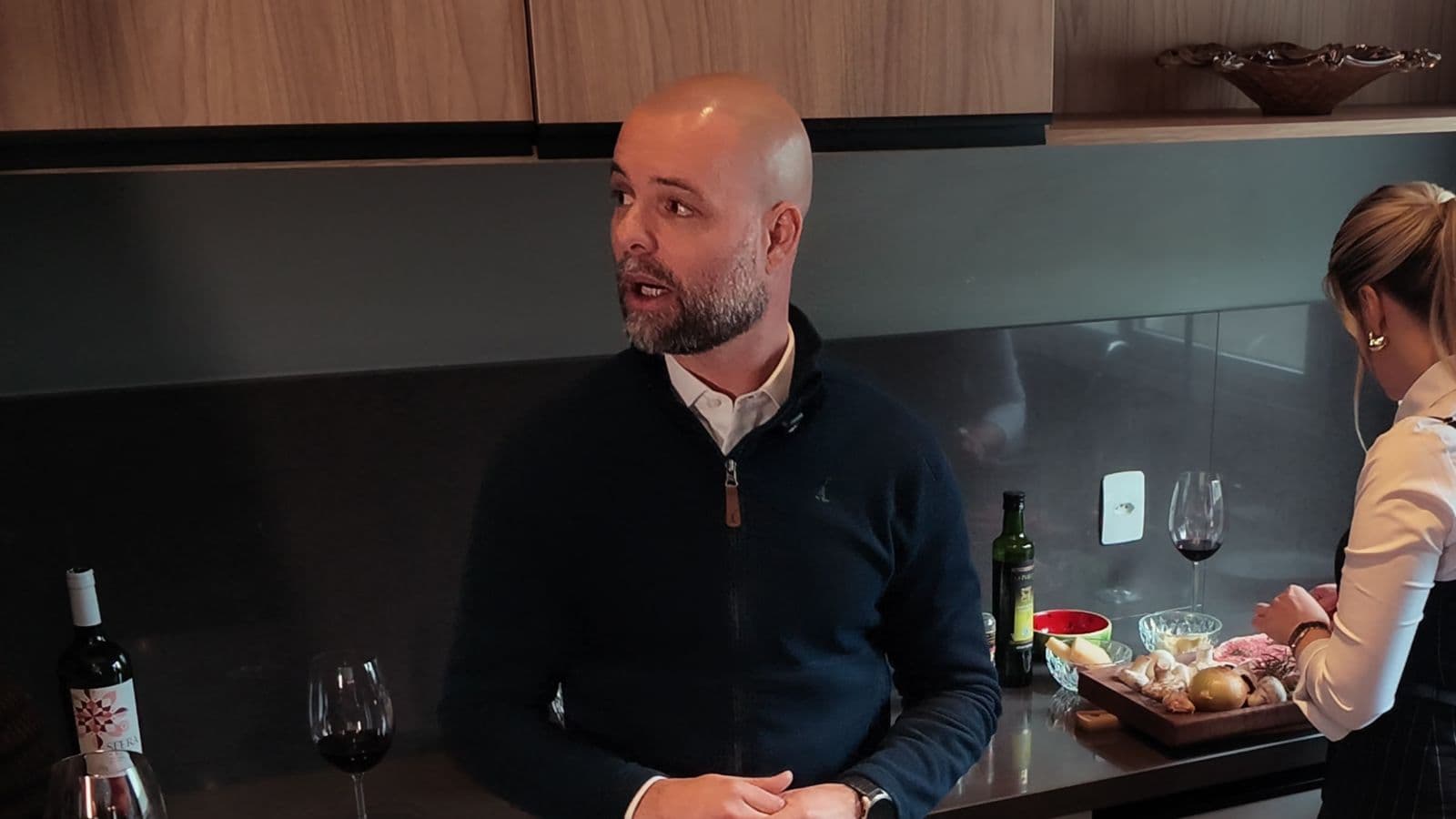 Paulo conversa na cozinha enquanto Joceane prepara a receita ao fundo