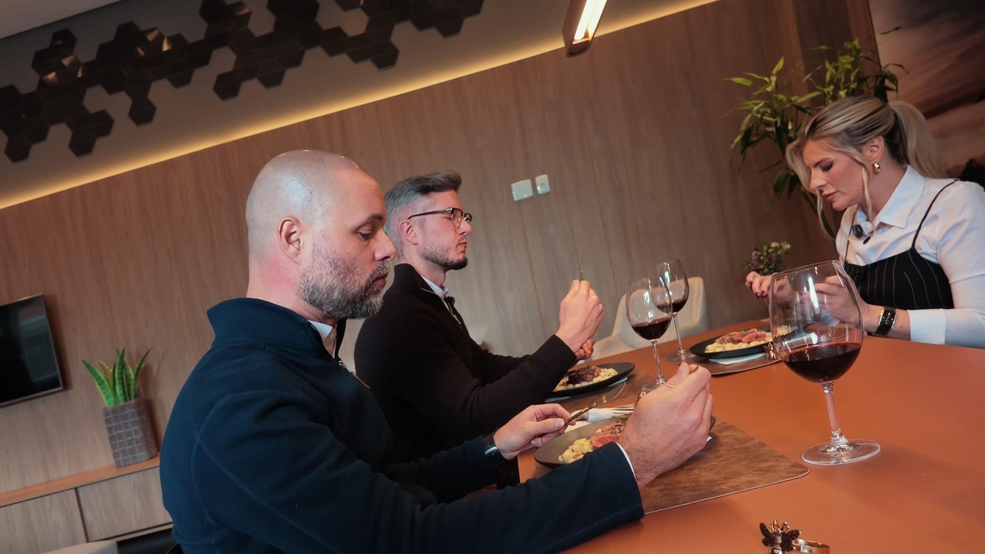 Paulo, Ícaro e Joceane jantam à mesa com taças de vinho tinto